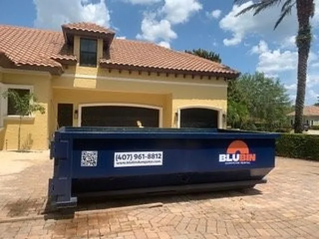 Blue BluBin Dumpster Rental roll-off container in the driveway of a Mediterranean-style home in Orlando, Florida