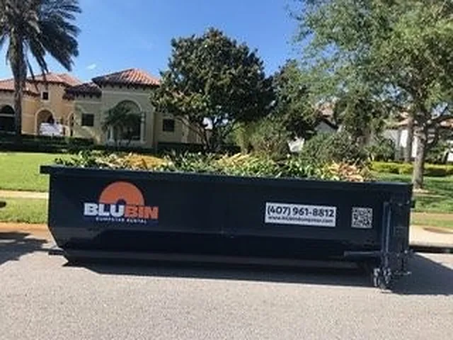 Blue BluBin Dumpster Rental roll-off container on a residential street lined with palm trees in Orlando, Florida