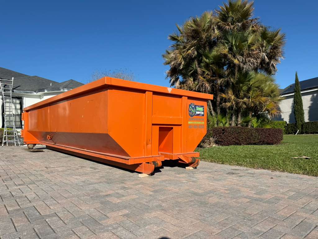 Orange Dumpster Strong 20-yard container staged on pavers under a Florida palm sky. Photo courtesy of Dumpster Strong.