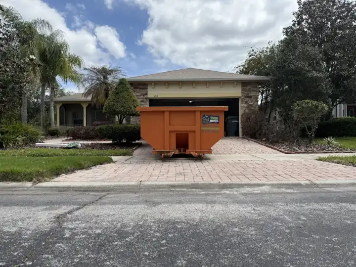 Orange Dumpster Strong roll-off container on a paver driveway in front of a house in Orlando, Florida