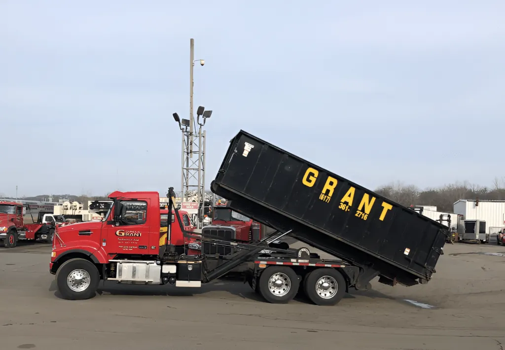 G. Grant red roll-off truck with hoisted black container at the company yard. Photo courtesy of G. Grant Industries.