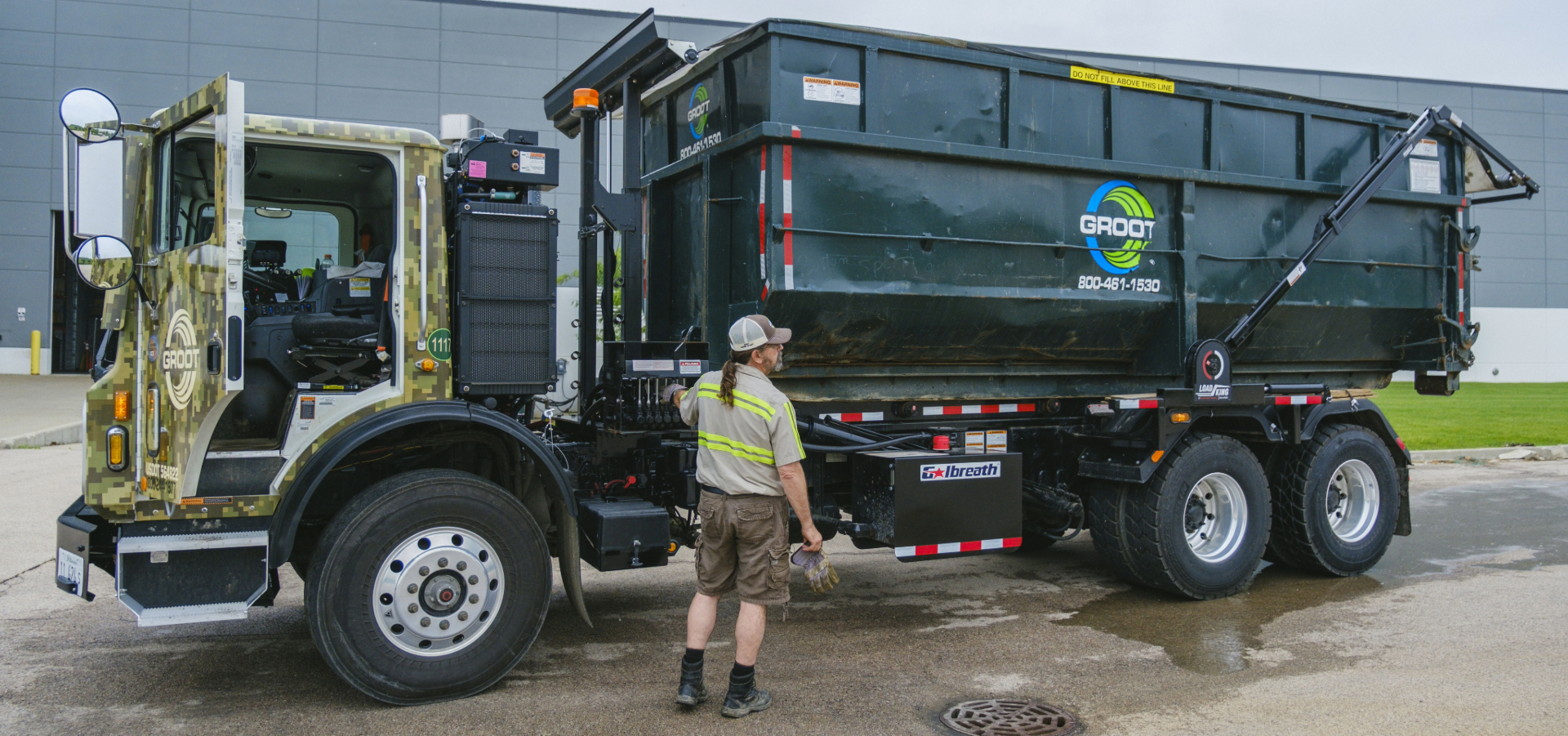 Groot camo-cab roll-off truck loaded with a black container at a clean facility lot. Photo courtesy of Groot.