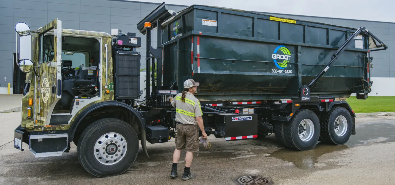 Groot camo-cab roll-off truck loaded with a black container at a clean facility lot. Photo courtesy of Groot.